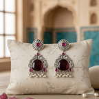 Pair of ornate earrings with red gemstones on a decorative pillow.