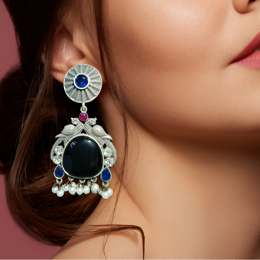 Close-up of a woman wearing an ornate earring with a blue gemstone on a pink background