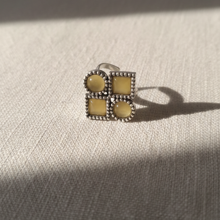 Silver ring with yellow gemstones on a textured beige surface