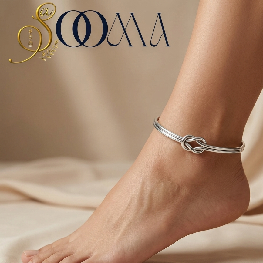 Side view of model foot wearing a sleek silver infinity knot dual-band ankle cuff on beige silk fabric