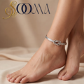 Close-up view of model feet adorned with a minimalist silver infinity knot open cuff anklet against beige backdrop