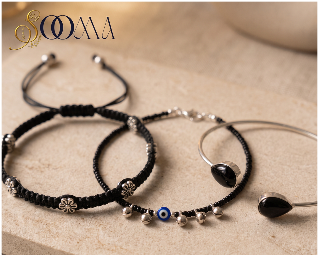 Sooma brand flat lay view of 3-piece ankle stack featuring floral macrame cord, blue Evil Eye ghungroo anklet, and black stone bypass cuff on stone surface
