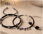 Sooma brand flat lay view of 3-piece ankle stack featuring floral macrame cord, blue Evil Eye ghungroo anklet, and black stone bypass cuff on stone surface