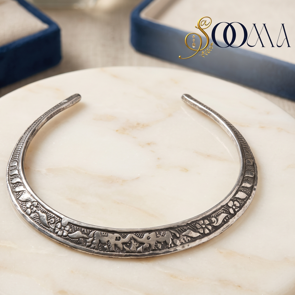 Sooma brand oxidized silver carved elephant Hasli necklace displayed flat on round white marble slab