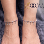 Front view of model's feet wearing pair of delicate silver elephant charm payal anklets on soft grey fabric