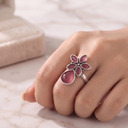 A silver flower-shaped ring with pink gemstones worn on a person's hand, resting on a light marble surface.