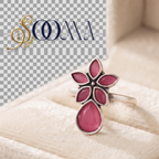 A silver ring with a flower-shaped setting and a teardrop-shaped pink stone, displayed inside a cream-colored jewelry box. A logo watermark for 'S.