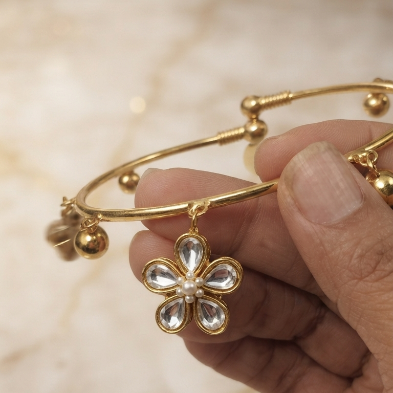 Hand holding gold flexible payal highlighting the 5-petal Kundan stone flower charm detail
