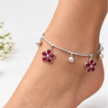 Model foot wearing silver flexible anklet with ruby red stone flower charms and silver ghungroos on brick background