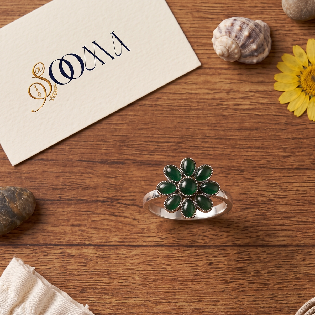 Sooma brand handcrafted oxidized silver green onyx 8-petal floral toe ring displayed flat on wooden surface with decorative stones