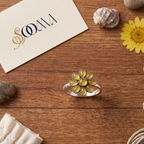 Sooma brand handcrafted oxidized silver yellow onyx 8-petal floral toe ring displayed flat on wooden surface with decorative stones