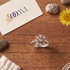 Sooma brand handcrafted oxidized silver green pink 8-petal floral toe ring displayed flat on wooden surface with decorative stones