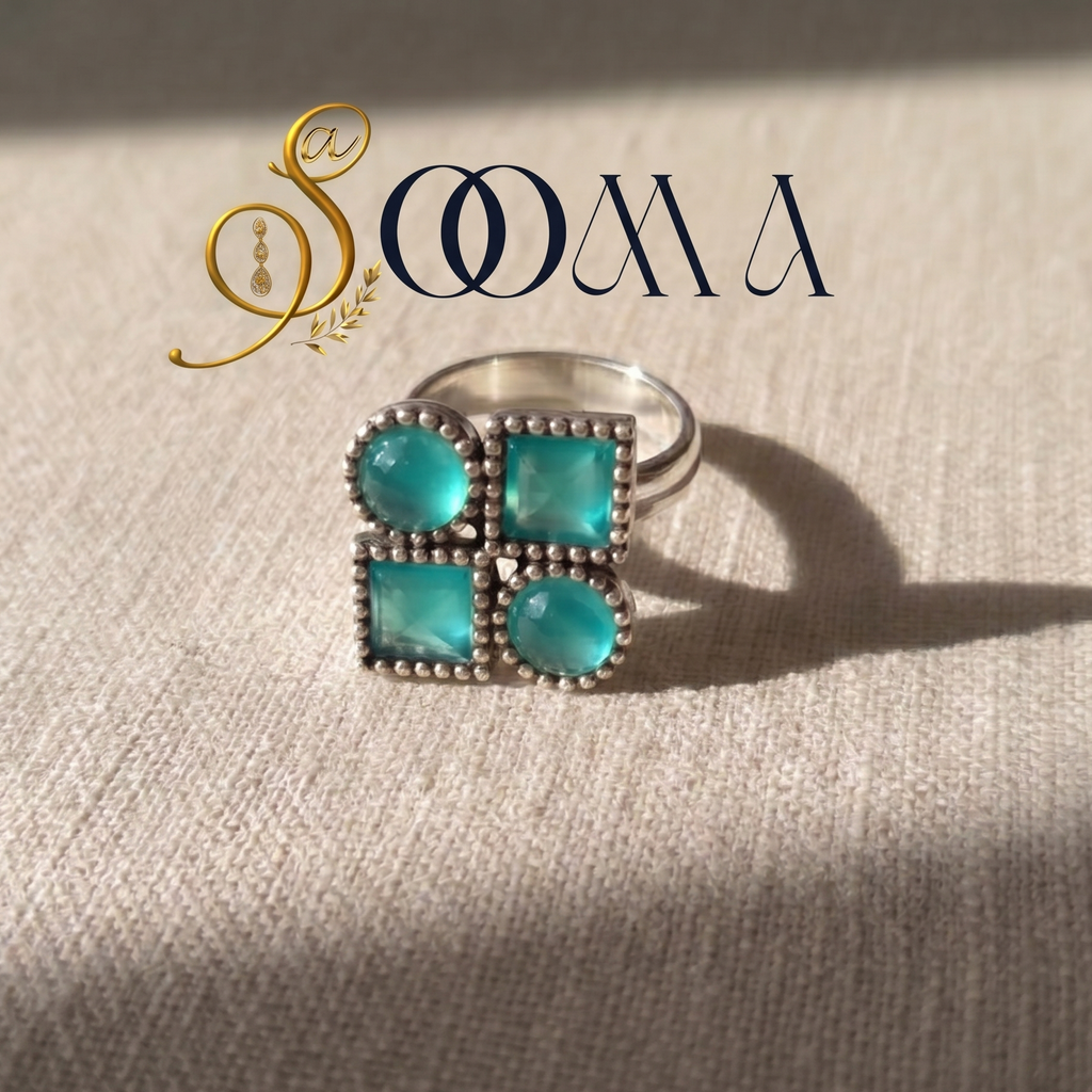 Silver ring with turquoise stones on a textured beige surface, featuring the brand 'Sooma'.