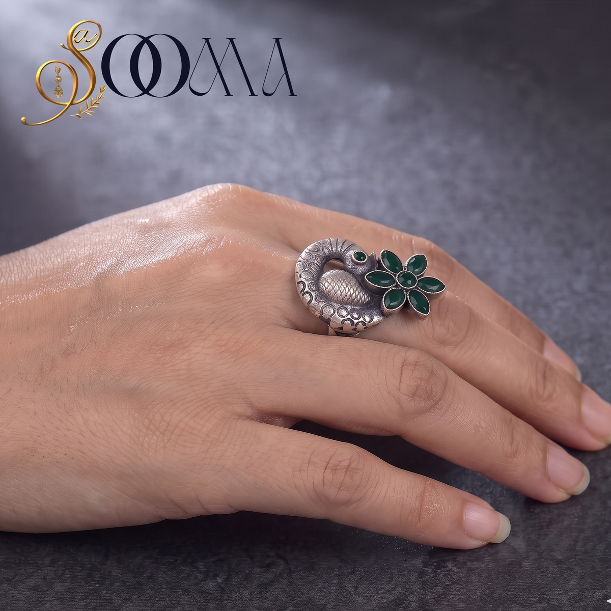 Side view of model hand styling an oxidized silver peacock statement ring with a green onyx flower crown on dark slate surface