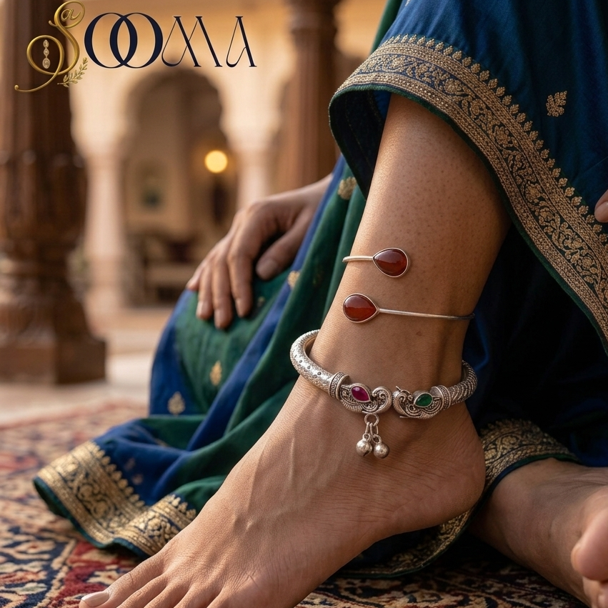 Close-up view of woman's foot adorned with a heavy silver peacock ghungroo kada and red stone bypass cuff against traditional rug