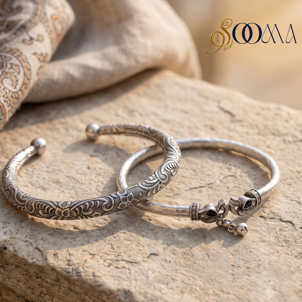 Sooma brand flat lay display of 2-piece silver ankle stack featuring an engraved filigree floral cuff and carved peacock ghungroo HASLI kada on sandstone