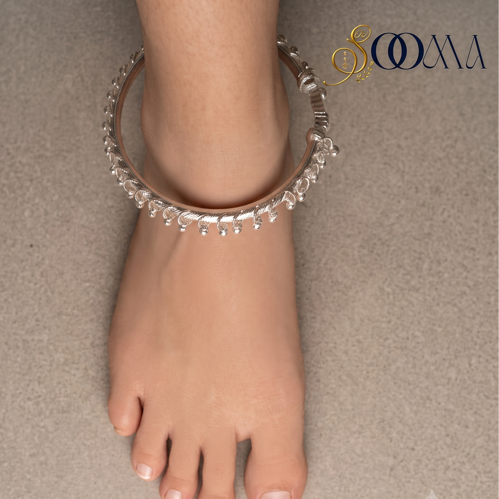 Top-down perspective of foot wearing rigid silver ghungroo ankle kada with hanging bead drops