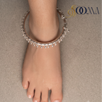 Top-down perspective of foot wearing rigid silver ghungroo ankle kada with hanging bead drops