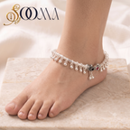 Top-down perspective of foot wearing rigid silver ghungroo ankle kada with hanging bead drops