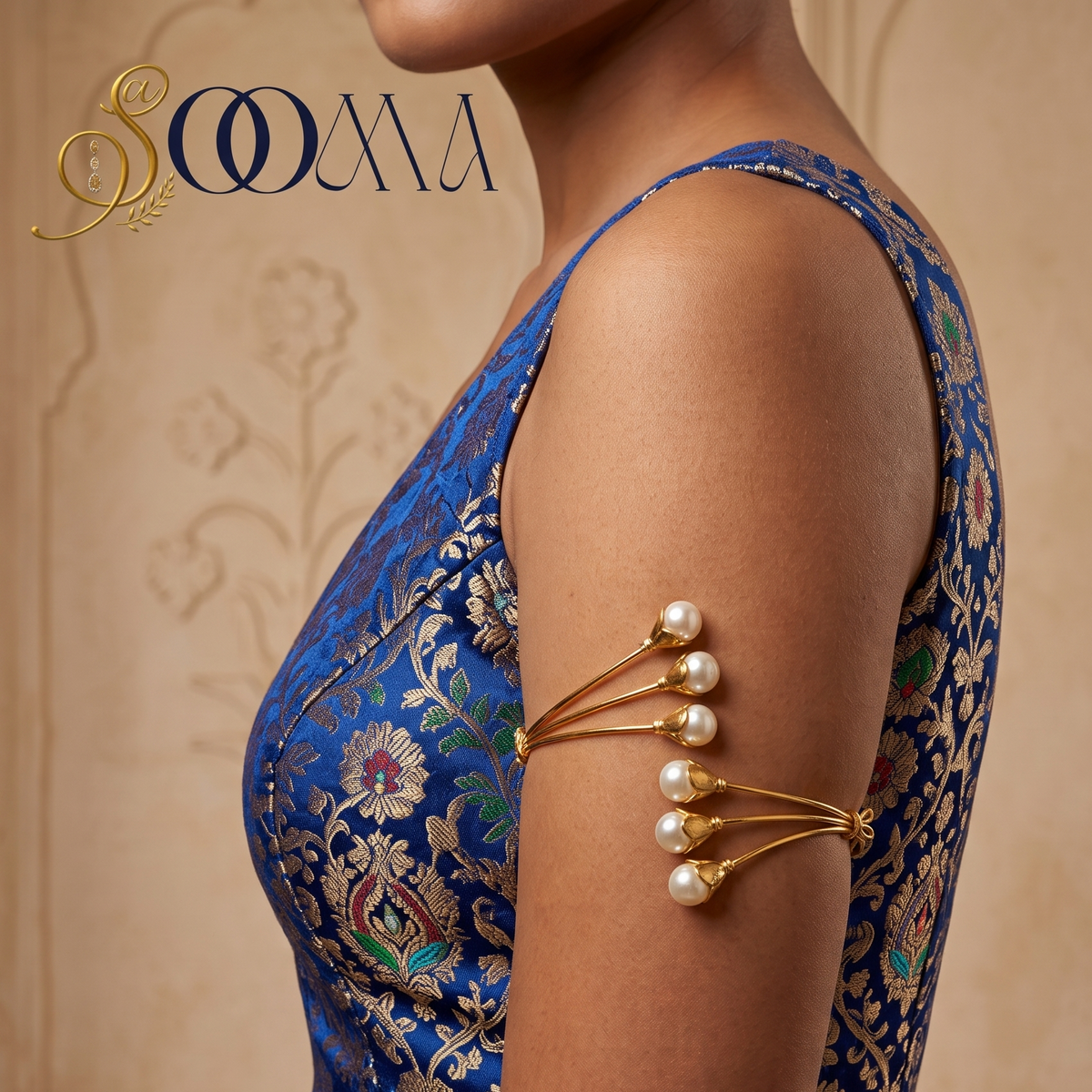 A woman shown from the side wearing a blue floral embroidered blouse with a gold armband accessory featuring pearl-like beads. The background is a warm beige textured wall, and the brand logo 'SOOMA' is visible in the top left corner.
