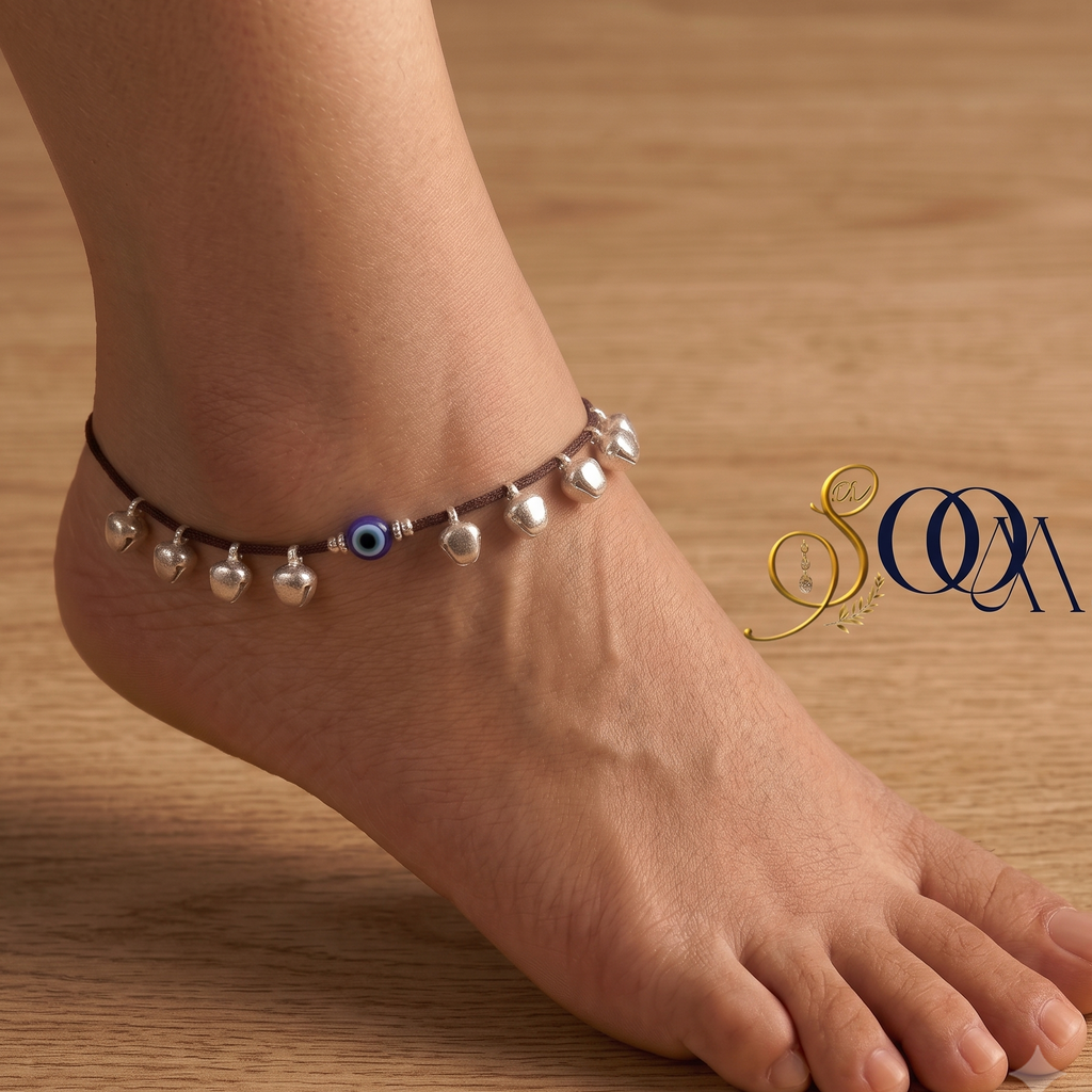 Side view of foot wearing black thread evil eye anklet with silver ghungroo drops on dark wooden floor
