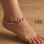 Side view of foot wearing black thread evil eye anklet with silver ghungroo drops on dark wooden floor