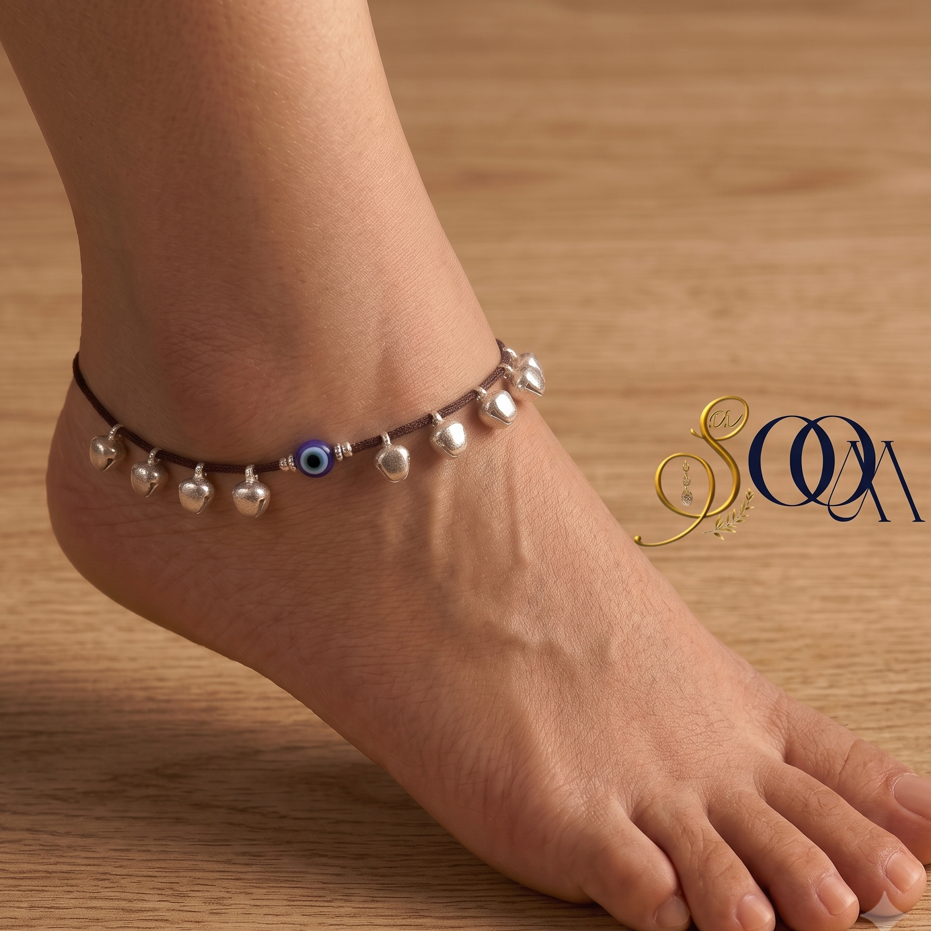 Side view of foot wearing black thread evil eye anklet with silver ghungroo drops on dark wooden floor