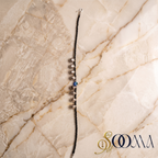Sooma brand black bead evil eye anklet with silver ghungroo bells displayed flat on marble