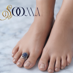 Close-up view of woman foot adorned with an adjustable oxidized silver blue stone floral toe ring on white marble surface