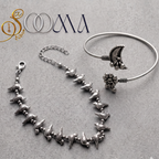 Sooma brand flat lay view of 2-piece silver ankle stack featuring bird charm chain anklet and crescent moon flower ghungroo bypass cuff on grey stone