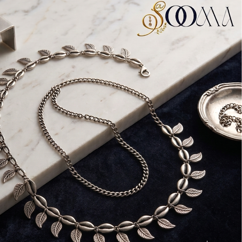 Sooma brand oxidized silver leaf and cowrie shell waist chain displayed flat on marble and dark blue velvet background
