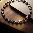 Sooma brand black cord anklet with continuous oxidized silver flower charms displayed flat on wooden tray
