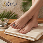A close-up lifestyle shot of a person's feet resting on a beige silk or satin fabric, with a prominent gray stone ring on the toes.