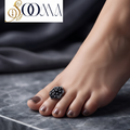 Side profile view of woman foot adorned with an adjustable blackened silver black stone shield toe ring on grey marble surface