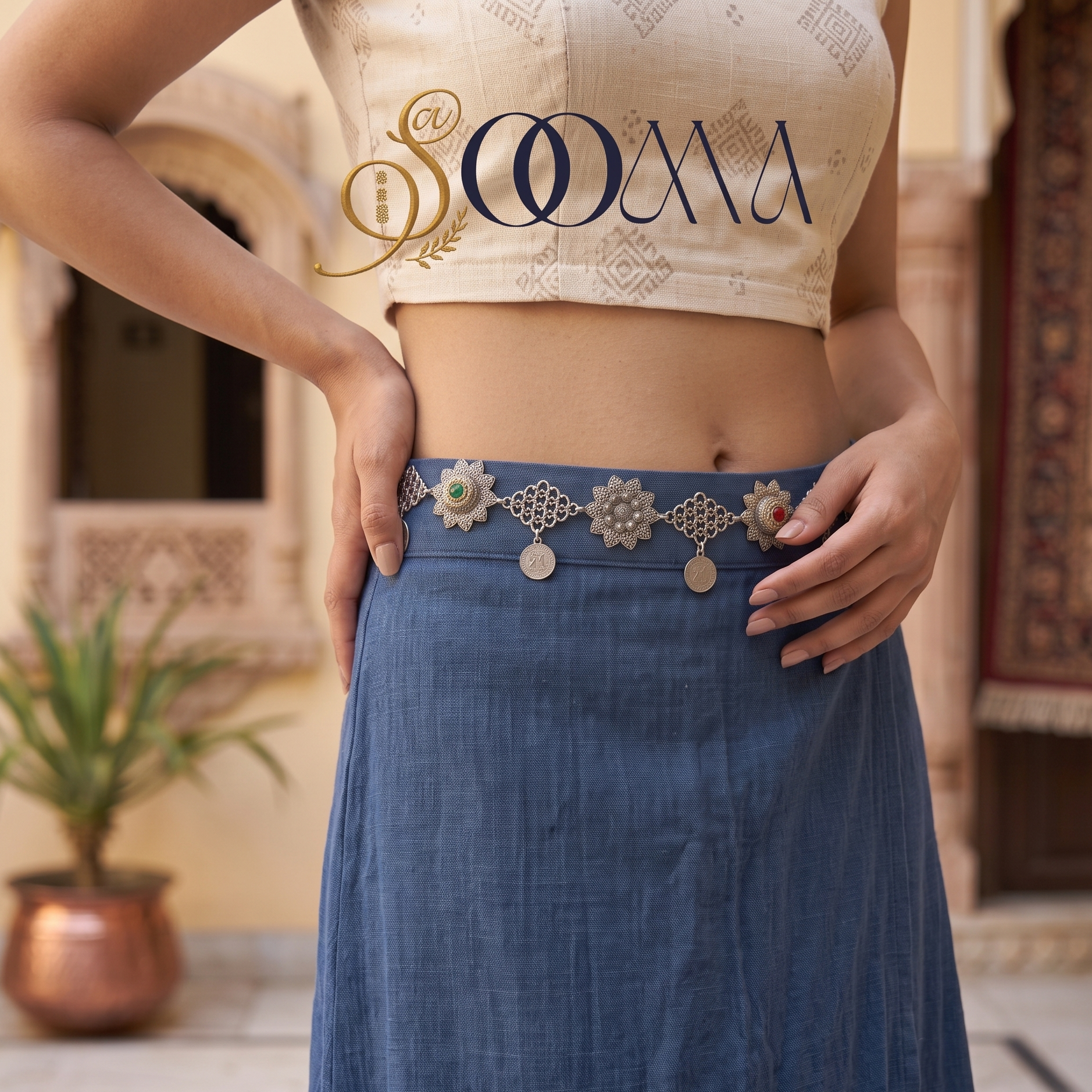Model posing in courtyard wearing handcrafted oxidized silver stone and coin waistbelt over blue skirt