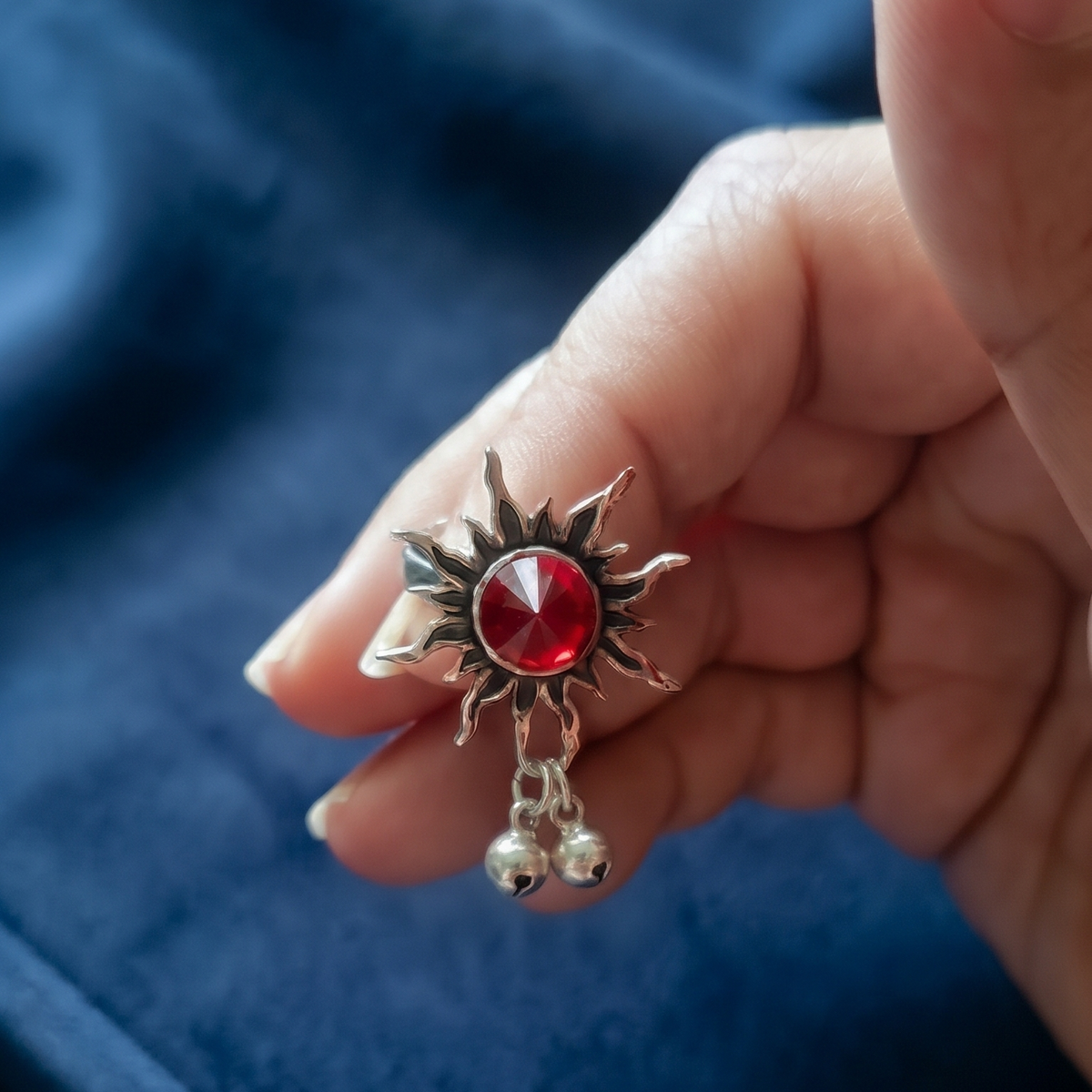 Hand holding Sooma brand oxidized silver ruby sunburst toe ring displaying the faceted red crystal and twin ghungroo drops
