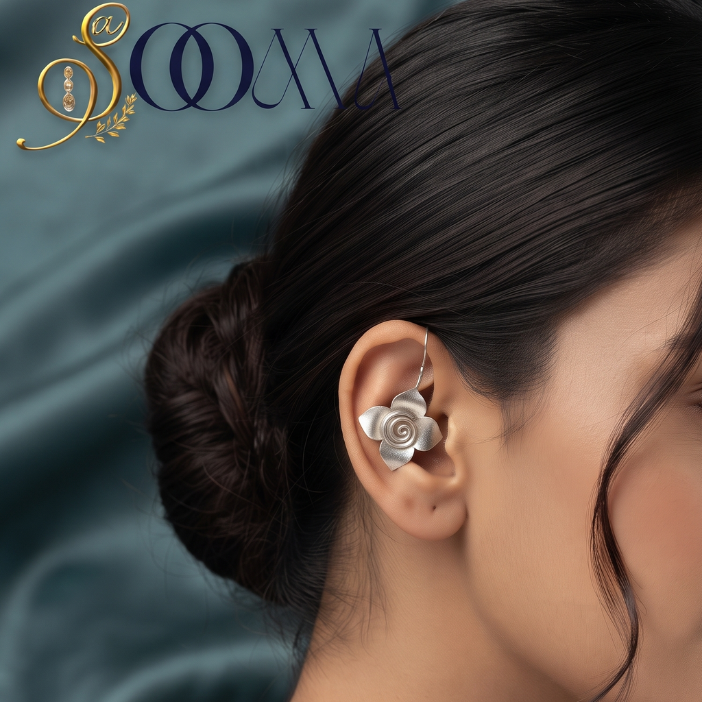 A close-up side profile of a woman with dark hair in a bun wearing a silver rose-shaped ear cuff. The background is a draped dark teal satin fabric, and the brand logo 'SCMA' is visible in the top left corner.
