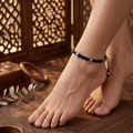 Side profile of foot wearing black macramé thread anklet with oxidized silver butterfly motifs