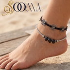 Close-up view of woman's ankle adorned with a 2-piece bohemian silver butterfly and black onyx bead anklet set on sandy backdrop