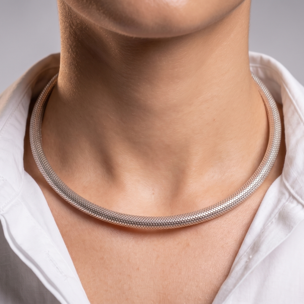 A close-up of a person's neck and collarbone area wearing a slim silver snake chain hasli necklace, paired with a white collared shirt against a soft gray studio background.