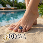 Model wearing an adjustable oxidized silver floral toe ring with deep blue stones on a sandy beach next to a swimming pool
