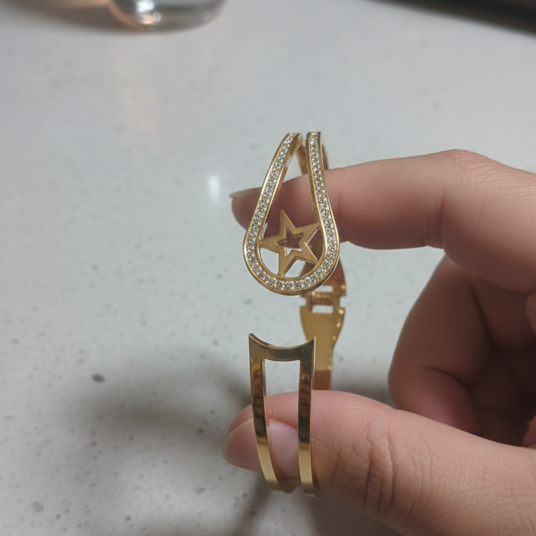 Gold bracelet held by a hand on a light surface with a small bottle in the background