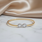 Gold bracelet with an infinity symbol on a marble surface with beige fabric in the background