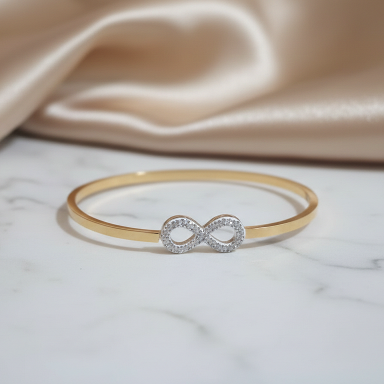 Gold bracelet with an infinity symbol on a marble surface with beige fabric in the background