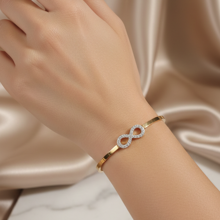 Hand wearing gold bracelet with an infinity symbol on a marble surface.