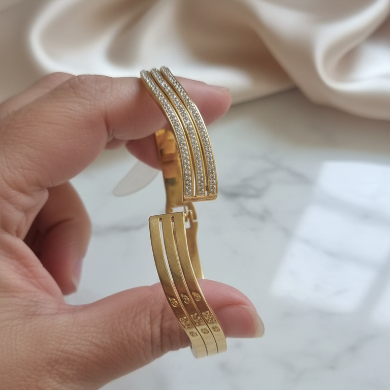 Gold bracelet held by a hand on a marble surface with a beige fabric background