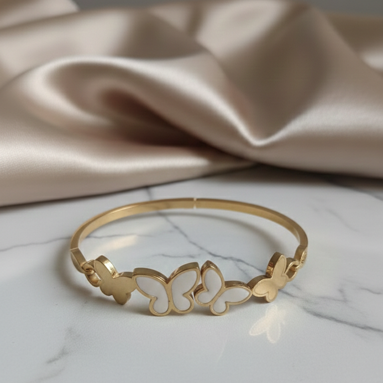 Gold bracelet with butterfly designs on a marble surface with a beige fabric background
