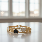 Gold bracelet with heart and black heart charms on a light surface with a blurred window background