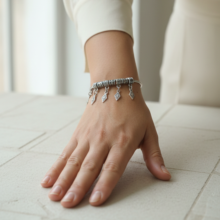 Hand wearing a silver charm bracelet on a light surface 