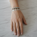 Hand wearing a silver charm bangle on a light background